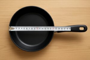 テーブルの上に置かれた黒いフライパンと、その上に伸ばされたメジャー。直径が測られ、サイズ感が分かりやすく表現されている。