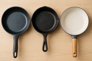 木目調のテーブルの上に並べられた三種類のフライパン。左からアルミ製、鉄製、セラミックコーティング製のフライパンがそれぞれ異なる質感を見せている。