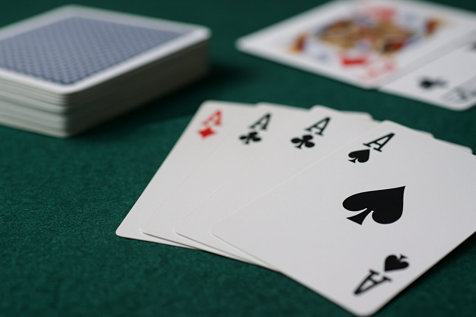 緑のフェルトの上に並べられた4枚のエースカード（スペード、クラブ、ダイヤ、ハート）が扇状に広がっている様子