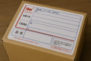 宅配便の伝票が貼られた段ボール箱のクローズアップ写真。品名欄が大きく表示されている。