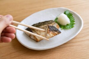 焼き魚の一切れを割り箸でつまんでいる場面のクローズアップ写真