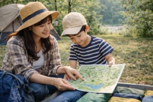キャンプ場で親子が地図を広げながら計画を立てている様子。必要な持ち物を考えながら、出発前の準備をしている風景。