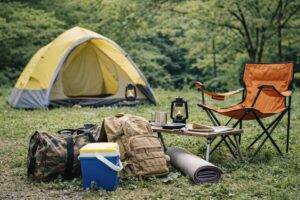キャンプ場のテーブル付近に、リュックや小さな収納ケースなど最低限の荷物がまとめて置かれている様子。日帰りキャンプの準備をイメージした風景。