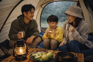小雨が降るキャンプ場で、テントの中に入り、外の様子を眺めながら過ごしている親子の様子。雨の日のキャンプの雰囲気を感じられる場面。